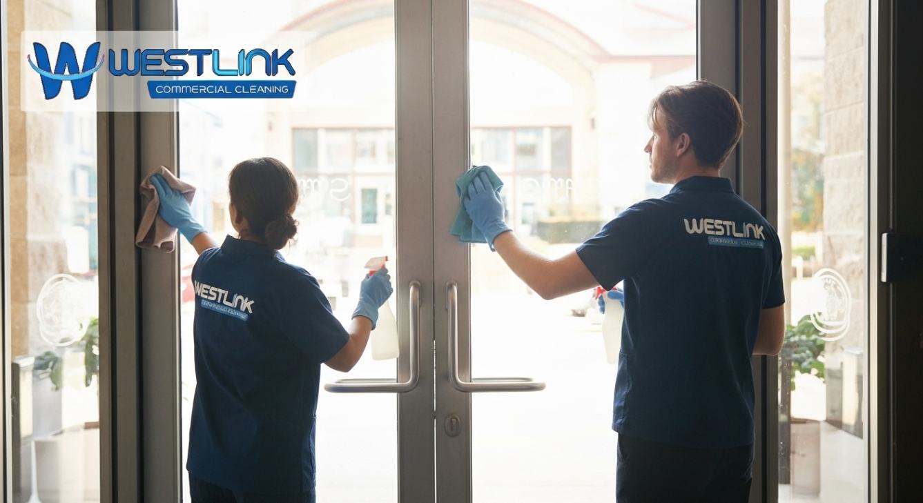 Commercial cleaners polishing laminated safety glass doors at a building entrance