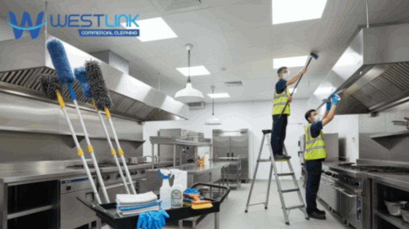 Commercial kitchen with ceiling fixtures being cleaned using professional tools and safety gear.