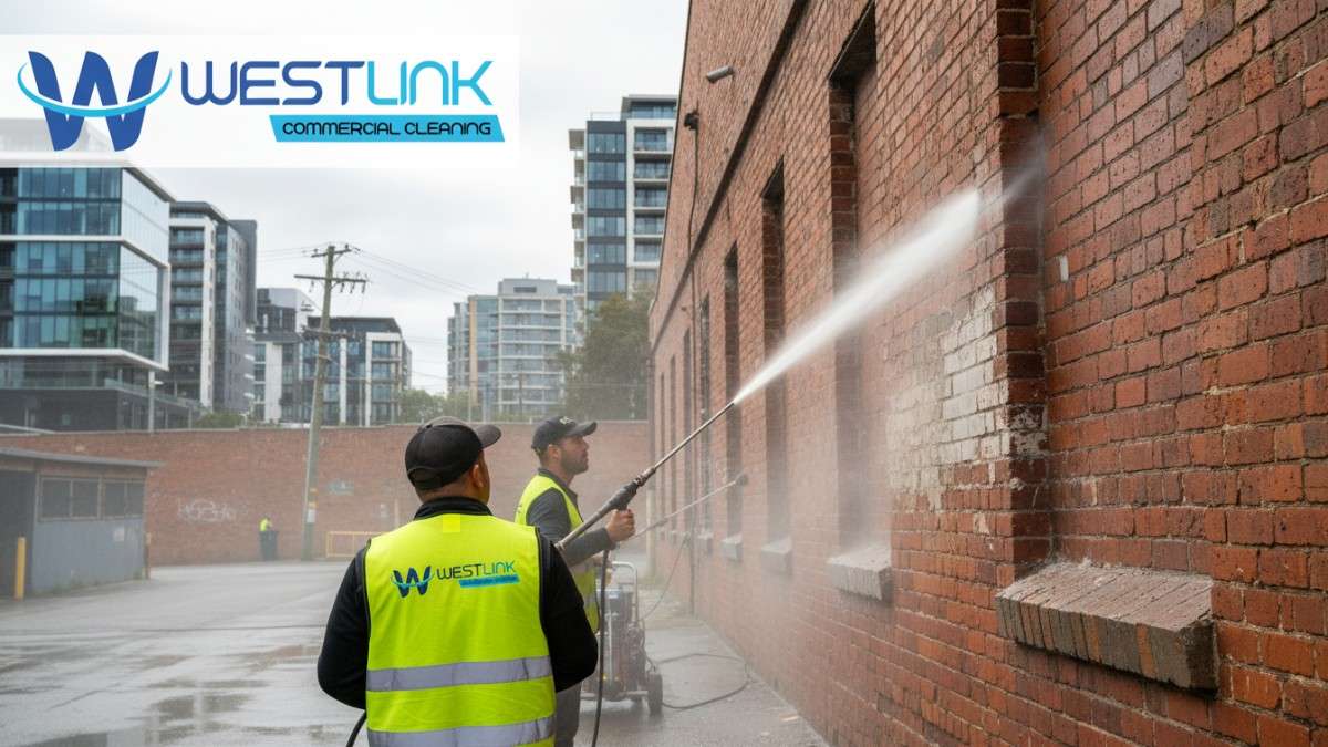 Workers pressure washing tag graffiti off a brick warehouse in Ultimo, with industrial urban backdrop.