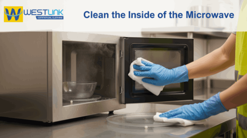 Gloved hands cleaning the interior of a commercial microwave with a microfiber cloth.