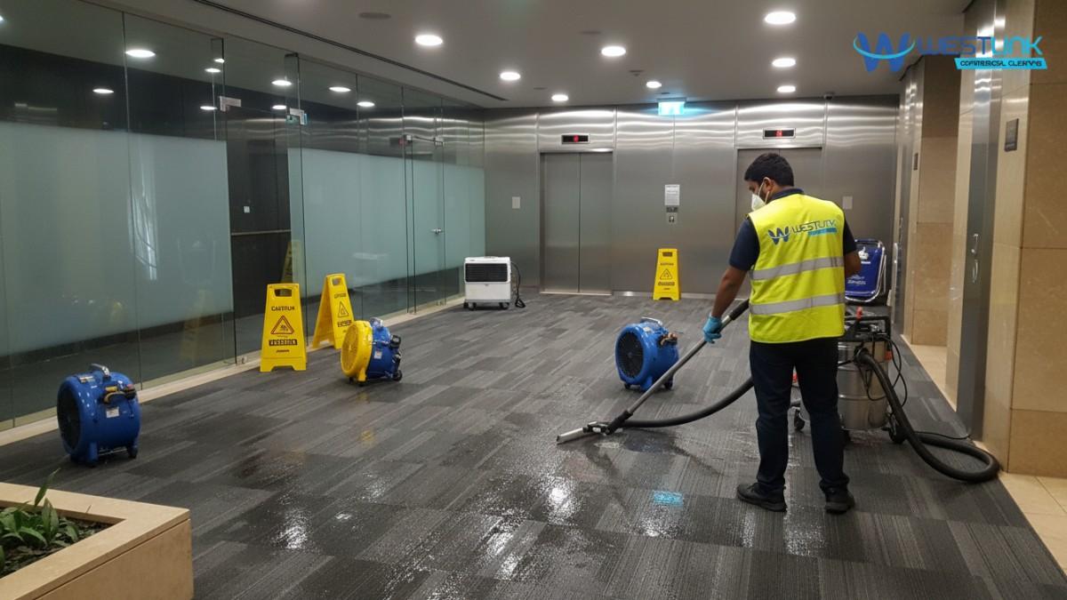 Technician extracting floodwater from carpet tiles in a Sydney CBD office lobby with air movers and dehumidifier.