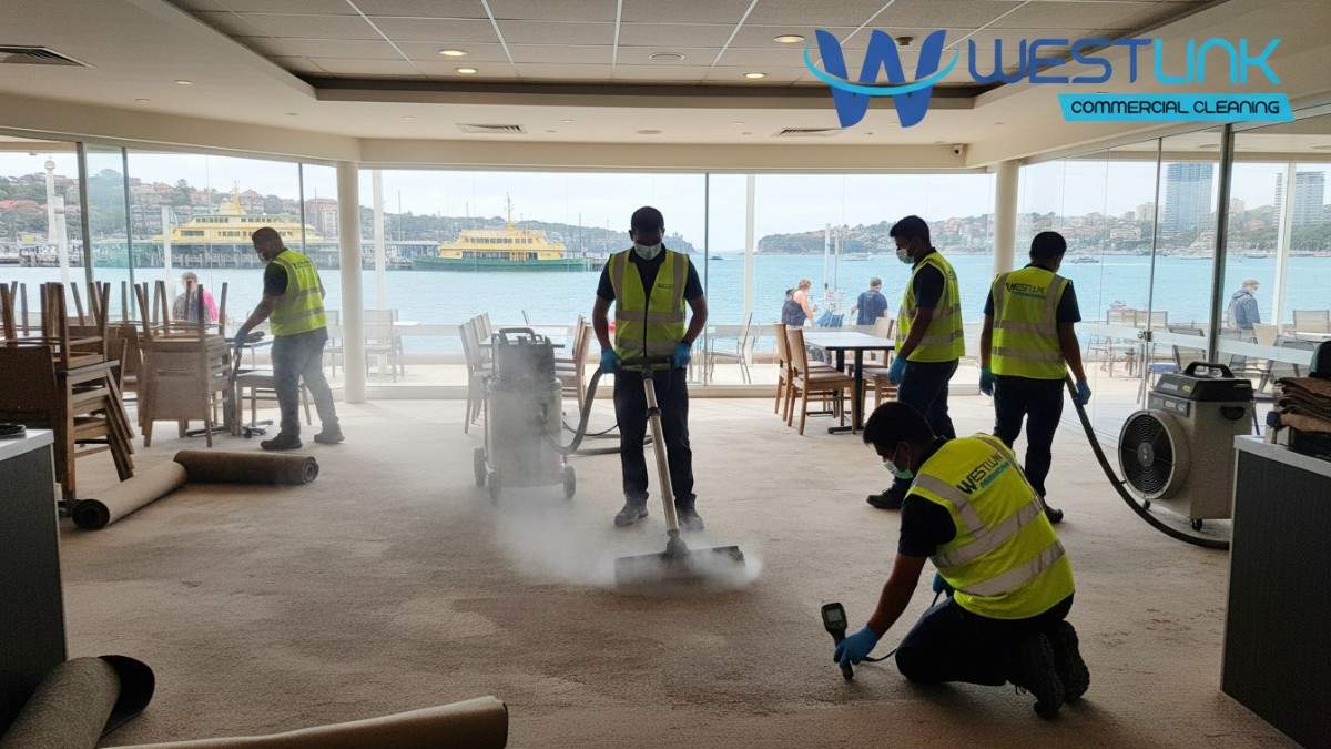 Team cleaning and restoring wet carpets in a Manly restaurant with steam equipment and meters.