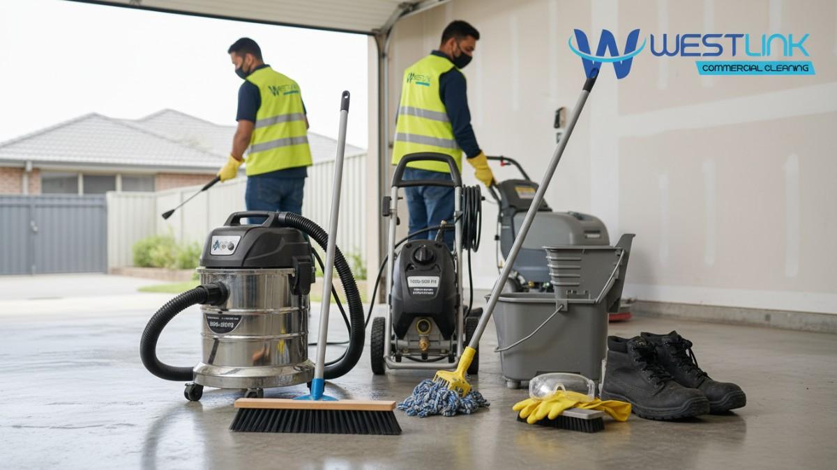 Arrangement of essential concrete cleaning tools including broom, vacuum, scrub brush, pressure washer, mop, scrubber, and protective gear on a garage floor.