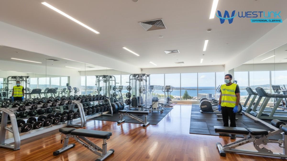 Pristine, professionally cleaned commercial gym interior in Newcastle, NSW, Australia, with polished floors, sanitized equipment, harbour views through windows.