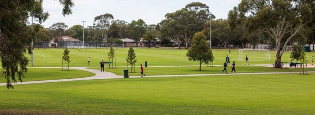Pristine community sports oval with green grass, walking paths, trees, and families enjoying the space