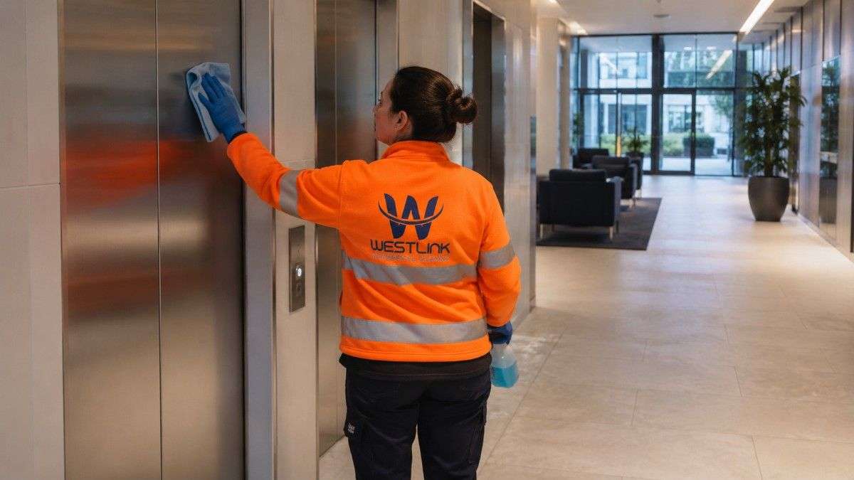 Westlink cleaner wiping stainless-steel elevator doors in a modern building foyer.